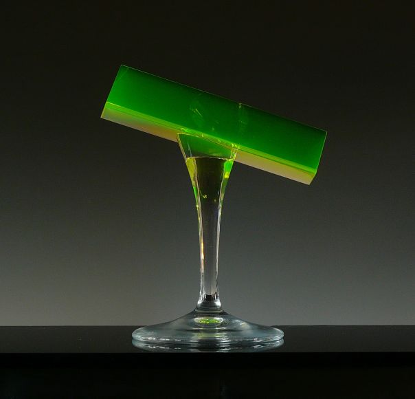 Titel: Atomic Green Design, utförande och foto: Anna Carlgren Material: Prismat är slipat och polerat av massivt uranhaltigt glas som limmats på en hyttarbetad fot av helkristall (33% blymönja, Pb3O4) Höjd: 15 cm Anna Carlgren slipar med kiselkarbid (SiC) på gjutjärnsskivor, finslipar med aluminiumoxid ( Al2O3)  och polerar på tagel med ceriumoxid (CeO2)